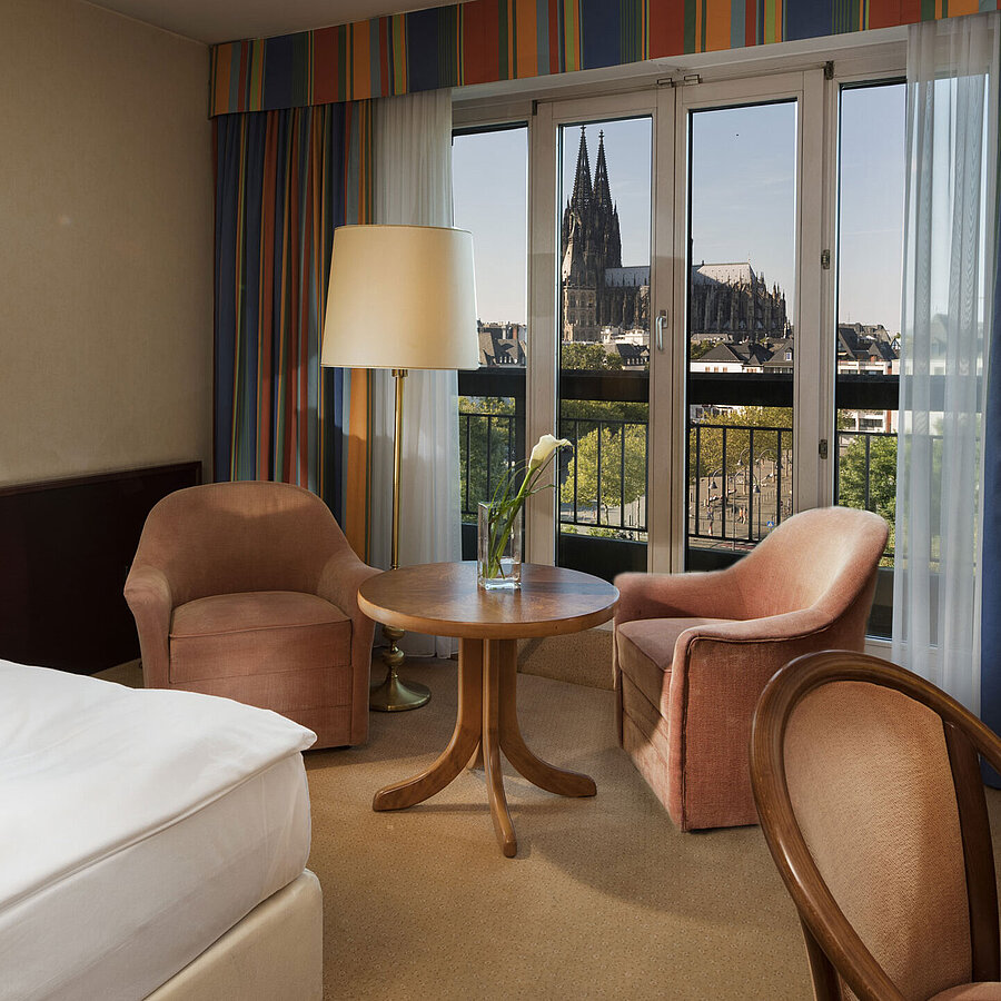 Chambre supérieure à l'hôtel Maritim Cologne avec coin salon, lit confortable et vue sur la cathédrale de Cologne.