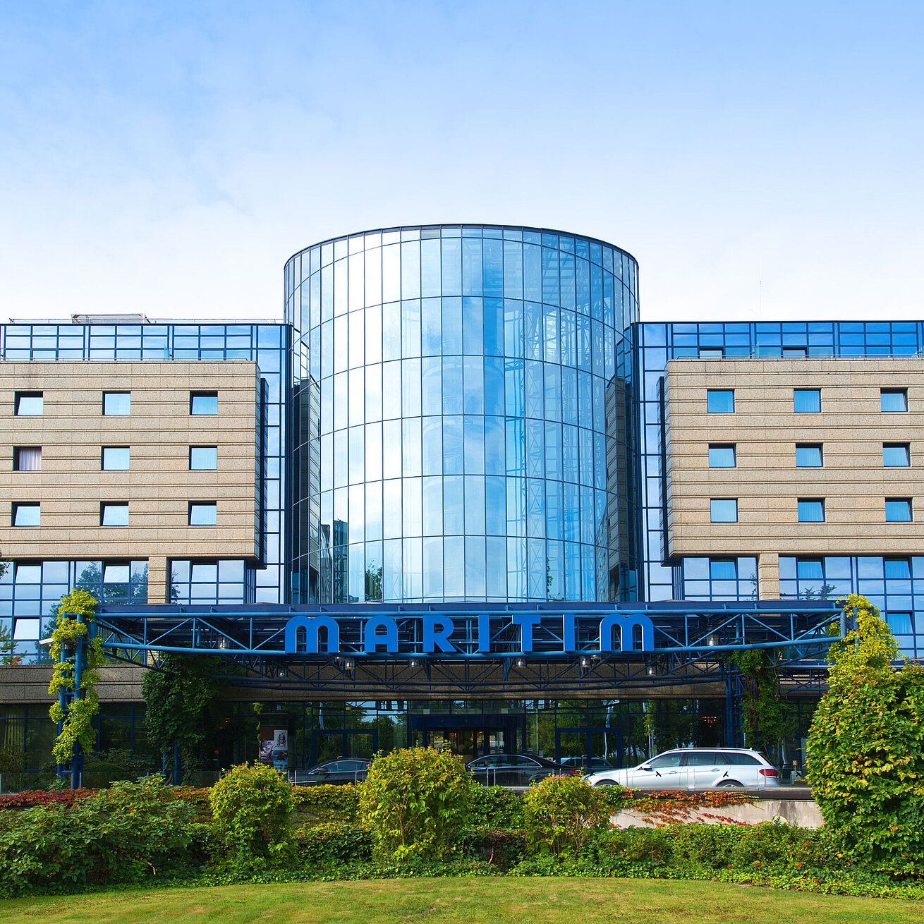 Exterior view of the Maritim Hotel Bonn with a modern glass facade and well-kept garden in the foreground.
