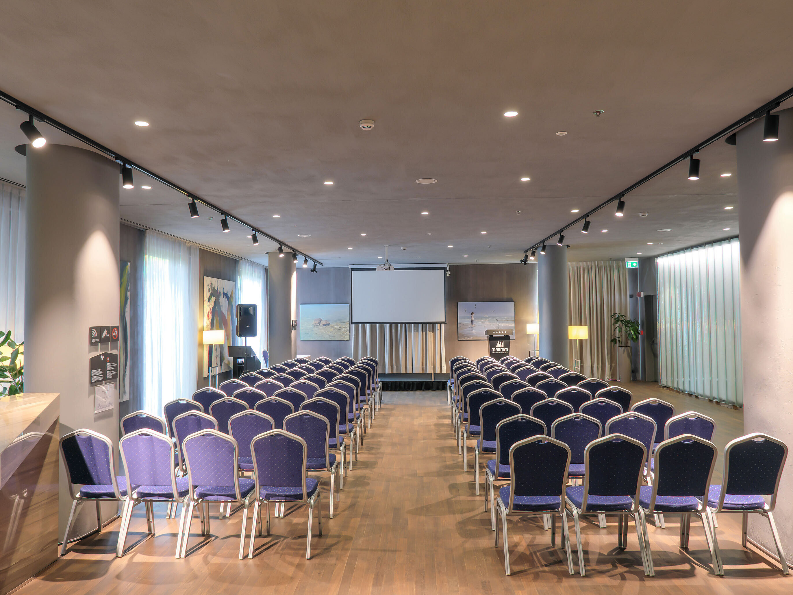 Sala luminosa en Maritim Hotel Plaza Tirana con butacas en filas y pantalla