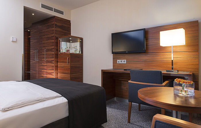Habitación moderna en el Maritim Hotel Múnich con zona de trabajo, TV, zona de estar y armario grande.