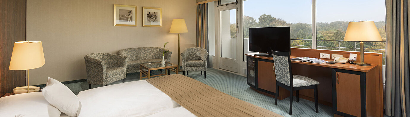 Camera comfort del Maritim Hotel Kiel con accogliente area salotto, scrivania, ampio letto e splendida vista sulla campagna.