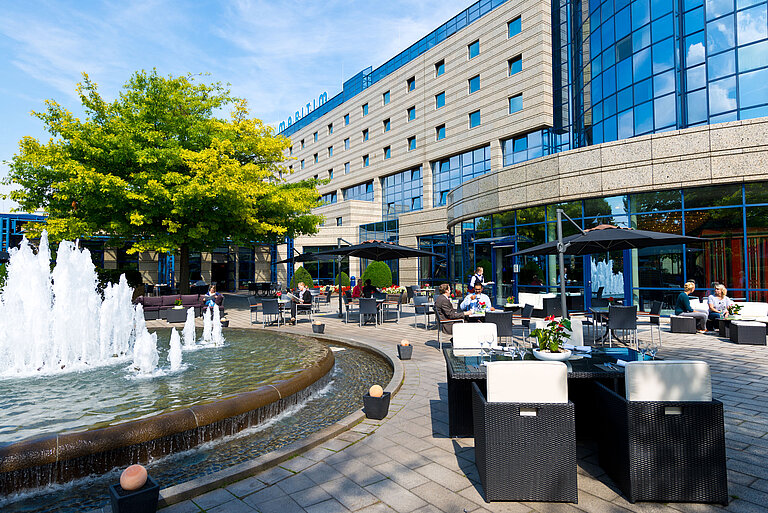 Terraza del Hotel Maritim Bonn con áreas de descanso, fuente y huéspedes cenando y relajándose al aire libre.