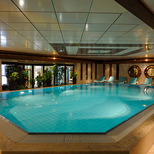 Piscina cubierta en el Hotel Maritim Colonia con tumbonas y plantas para un ambiente relajante.