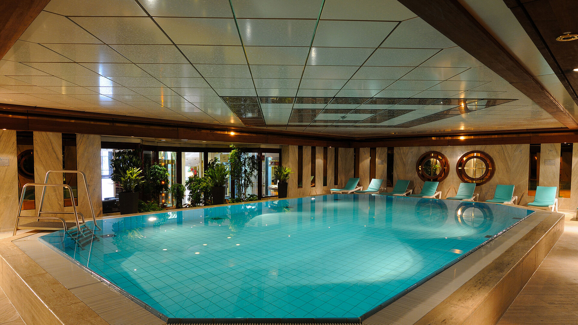 Piscina interna all'Hotel Maritim Colonia con lettini e piante per un'atmosfera rilassante.