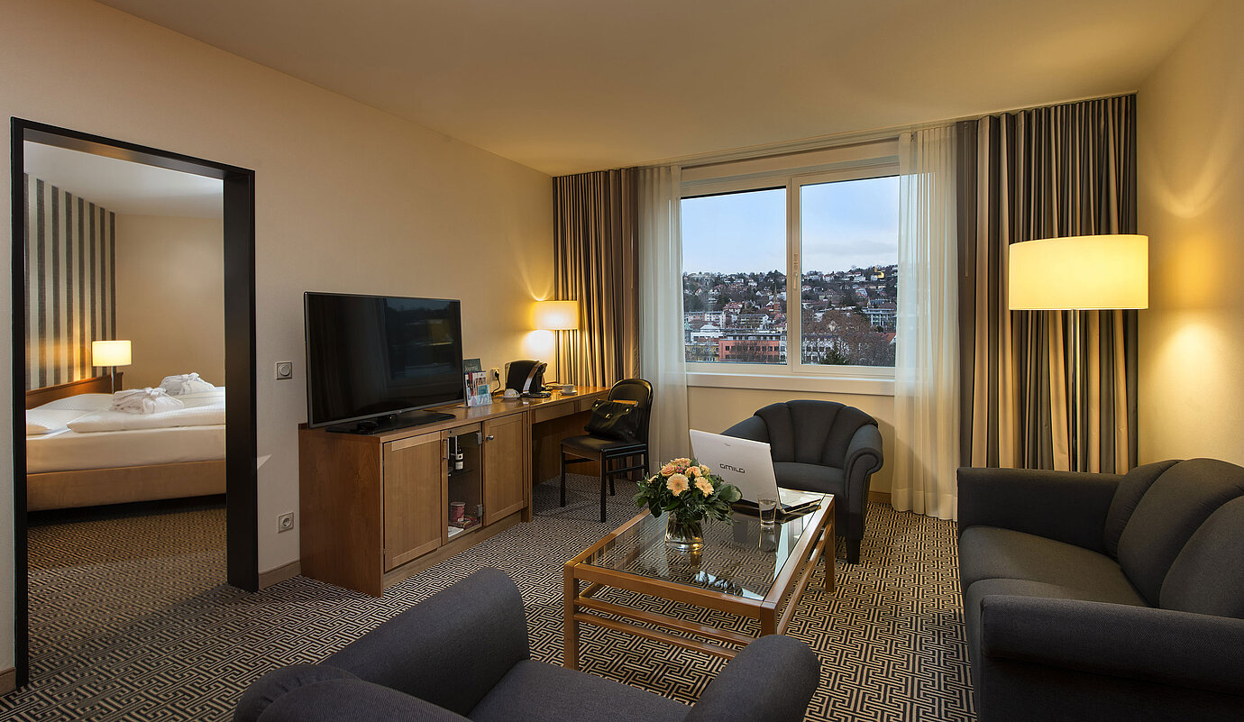 Living area with sofa, TV, desk and city view in the suite at the Maritim Hotel Stuttgart