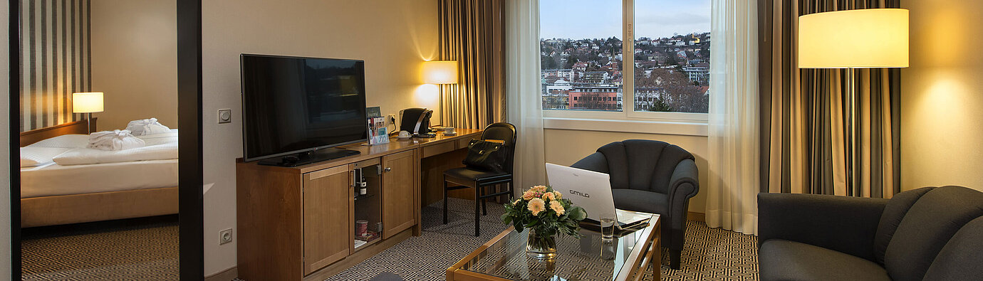 Living area with sofa, TV, desk and city view in the suite at the Maritim Hotel Stuttgart