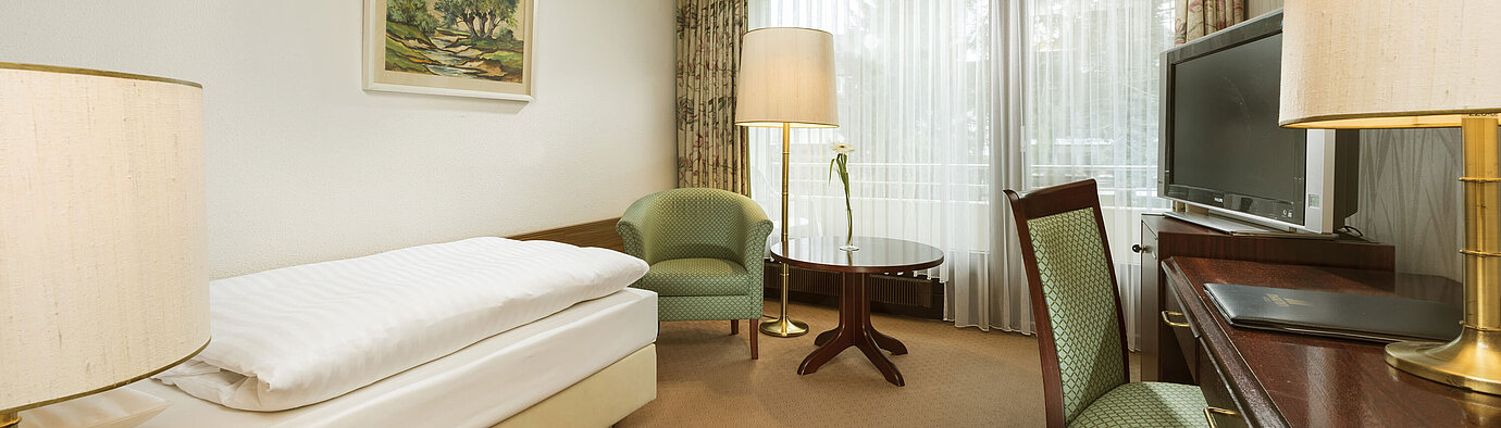 Habitación con escritorio, sillón y acceso al balcón en Maritim Hotel Bad Salzuflen