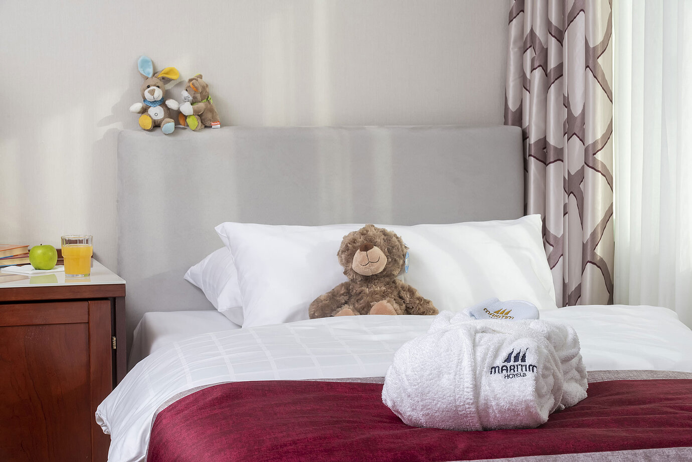 Suite familiar en el Hotel Maritim Bonn con cama acogedora, juguetes de peluche y albornoz, perfecto para niños.