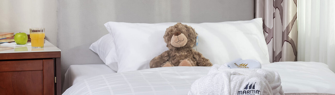 Suite familiar en el Hotel Maritim Bonn con cama acogedora, juguetes de peluche y albornoz, perfecto para niños.