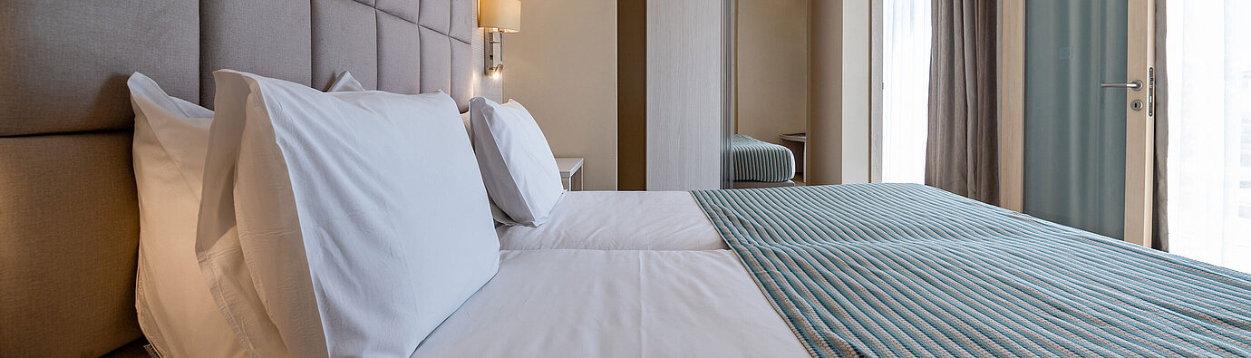 Suite Junior Elegante zona notte della Junior Suite del Maritim Antonine Hotel & Spa Malta con comodo letto matrimoniale, testiera imbottita, armadio moderno e finestre a tutta altezza.