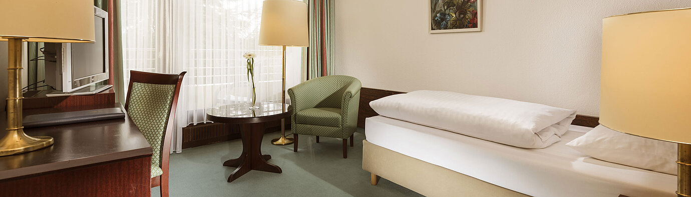 Habitación clara con sillón, escritorio y ventana en Maritim Hotel Bad Salzuflen