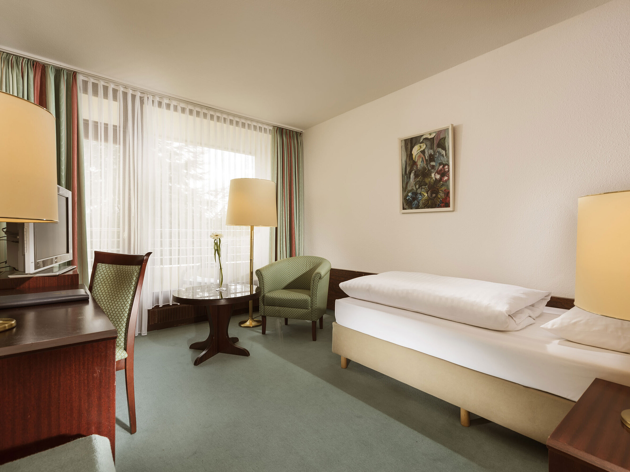 Bright single room with armchair, desk and large window at Maritim Hotel Bad Salzuflen