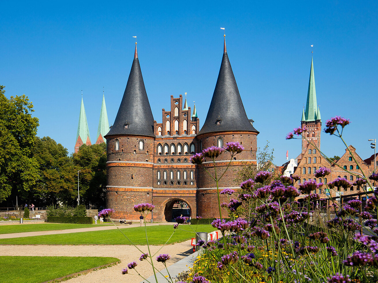 Holstentor Lúbeck Holstentor en Lübeck con flores floreciendo en primer plano y cielo azul.
