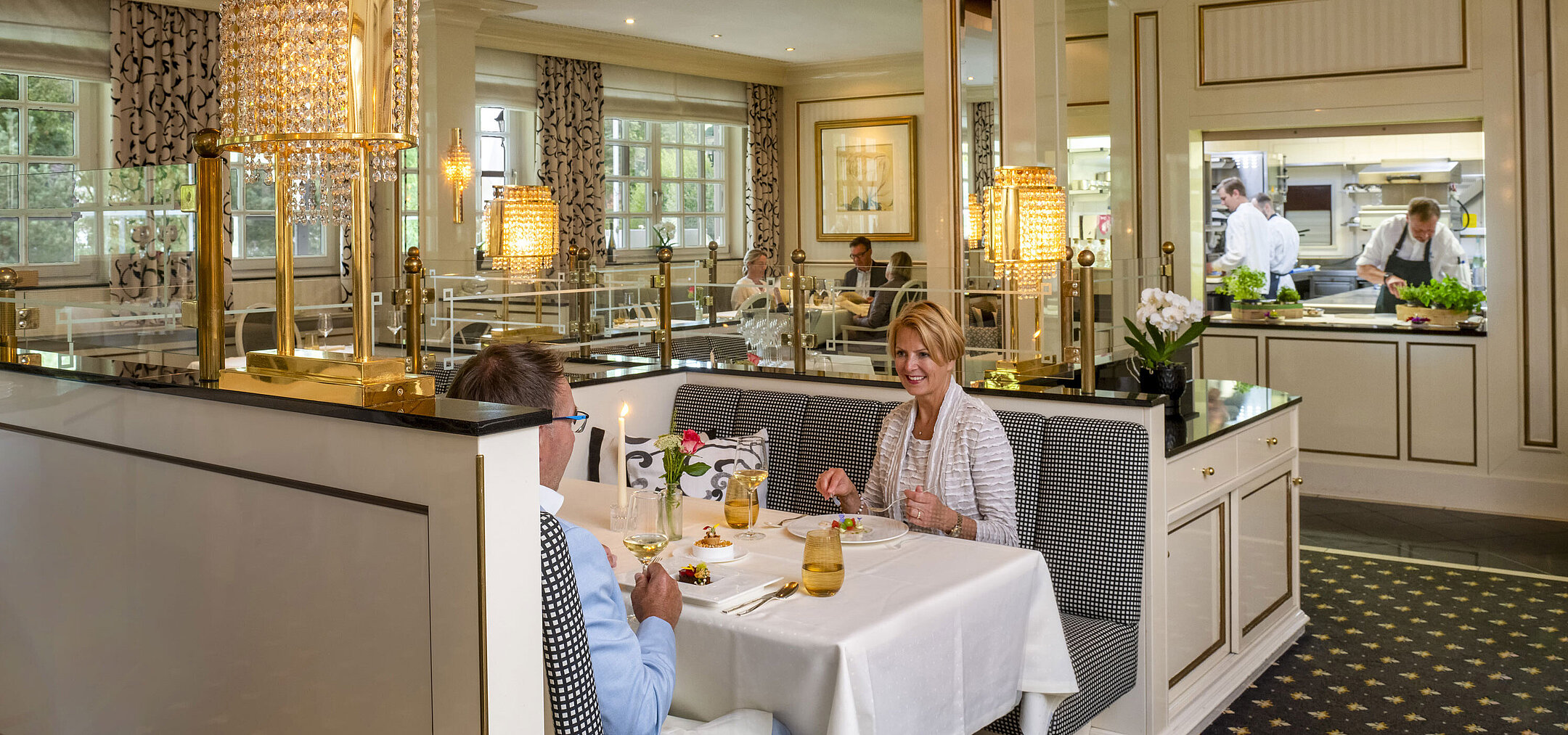 Couple profitant d'un dîner raffiné au restaurant Orangerie du Maritim Seehotel Timmendorfer Strand avec vue sur la cuisine.