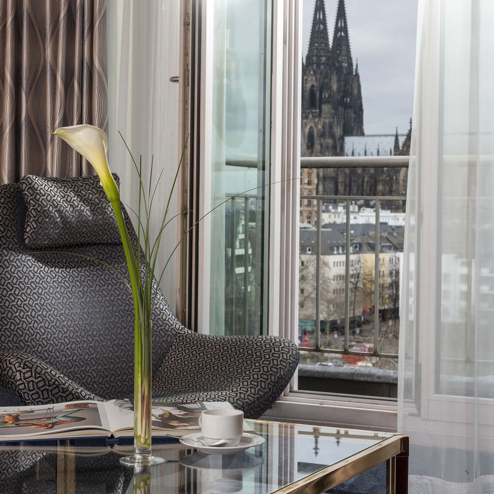 Junior Suite Junior Suite at Maritim Hotel Cologne with balcony view of Cologne Cathedral, modern chair, and coffee table with decoration.