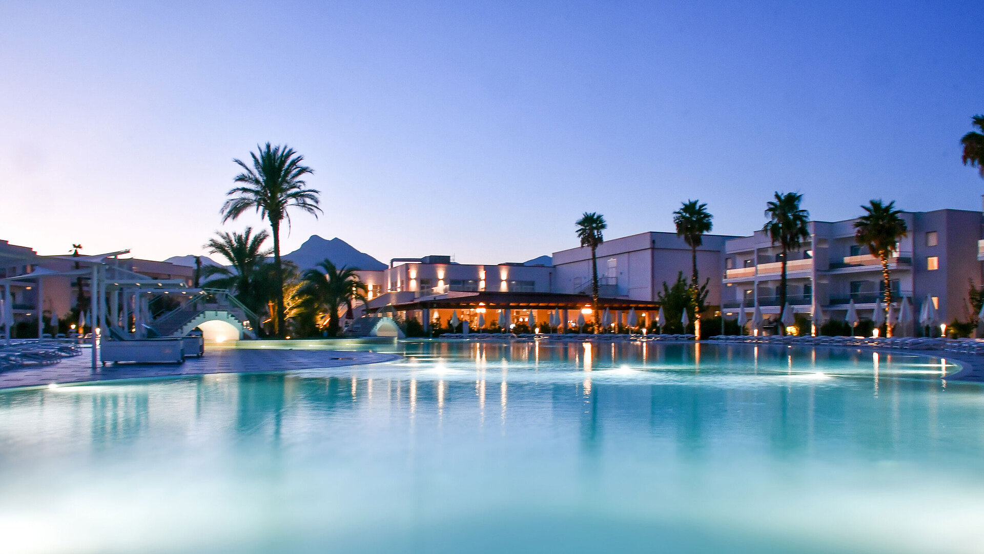 Luces nocturnas en la piscina del Maritim Resort Calabria con palmeras y montañas