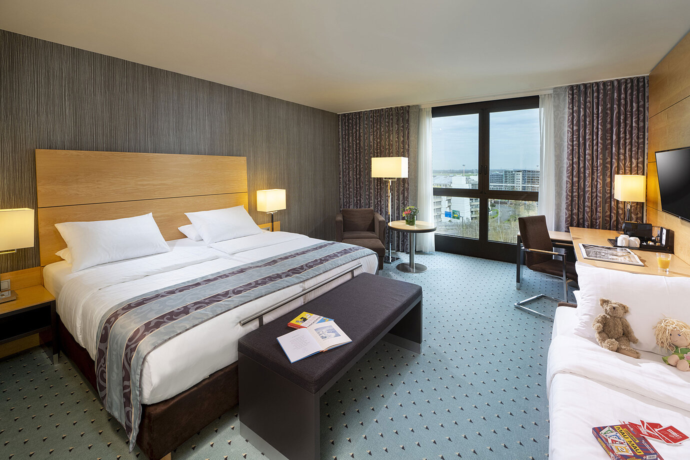 Amplia habitación familiar superior en el Maritim Hotel Düsseldorf con cama grande, cama adicional y vistas a la ciudad.