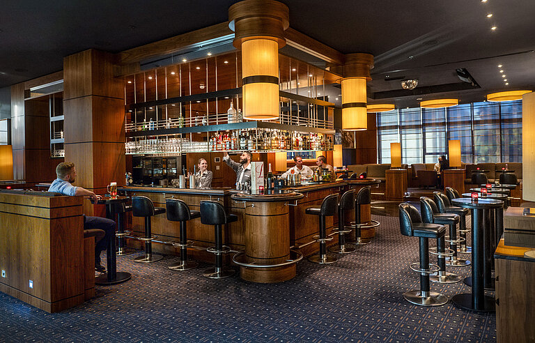 Elegante bar del hotel en el Maritim Hotel Düsseldorf con diseño moderno, ambiente acogedor y clientes en la barra.