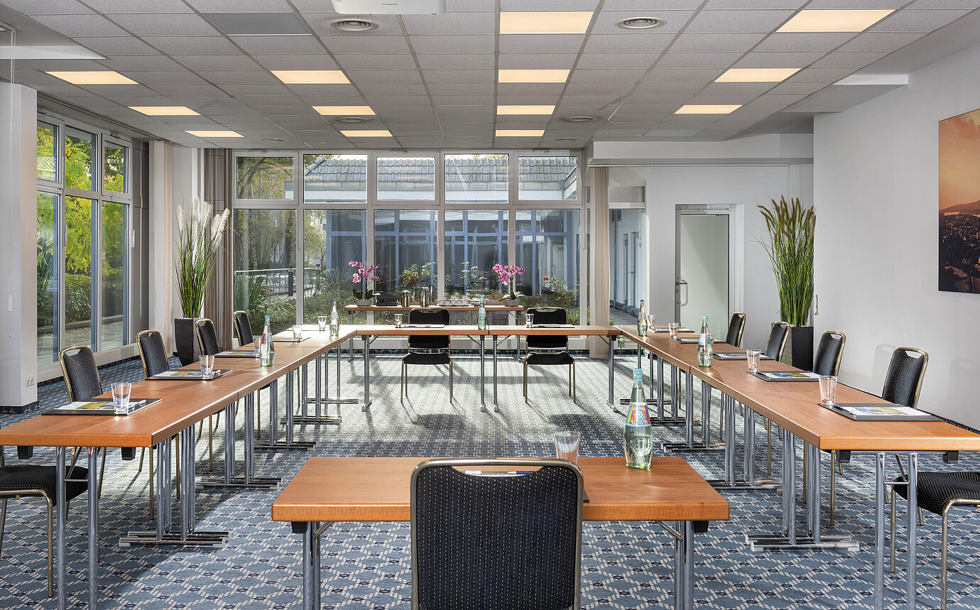 Salle de conférence lumineuse avec grandes fenêtres et vue sur la cour au Maritim Hotel Königswinter.