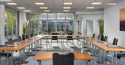 Salle de conférence lumineuse avec grandes fenêtres et vue sur la cour au Maritim Hotel Königswinter.