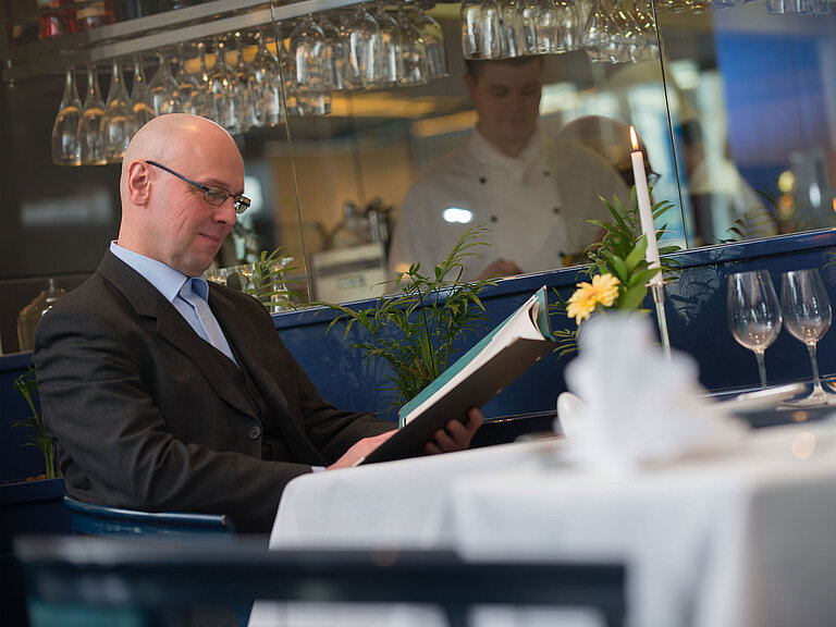 Ristorante Tavolo elegantemente apparecchiato nel ristorante dell'Hotel Maritim Magdeburgo con un ospite che consulta il menu.