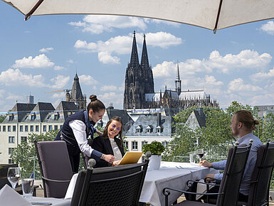 Los huéspedes disfrutan del servicio en la terraza del Hotel Maritim Colonia con vistas a la catedral de Colonia.