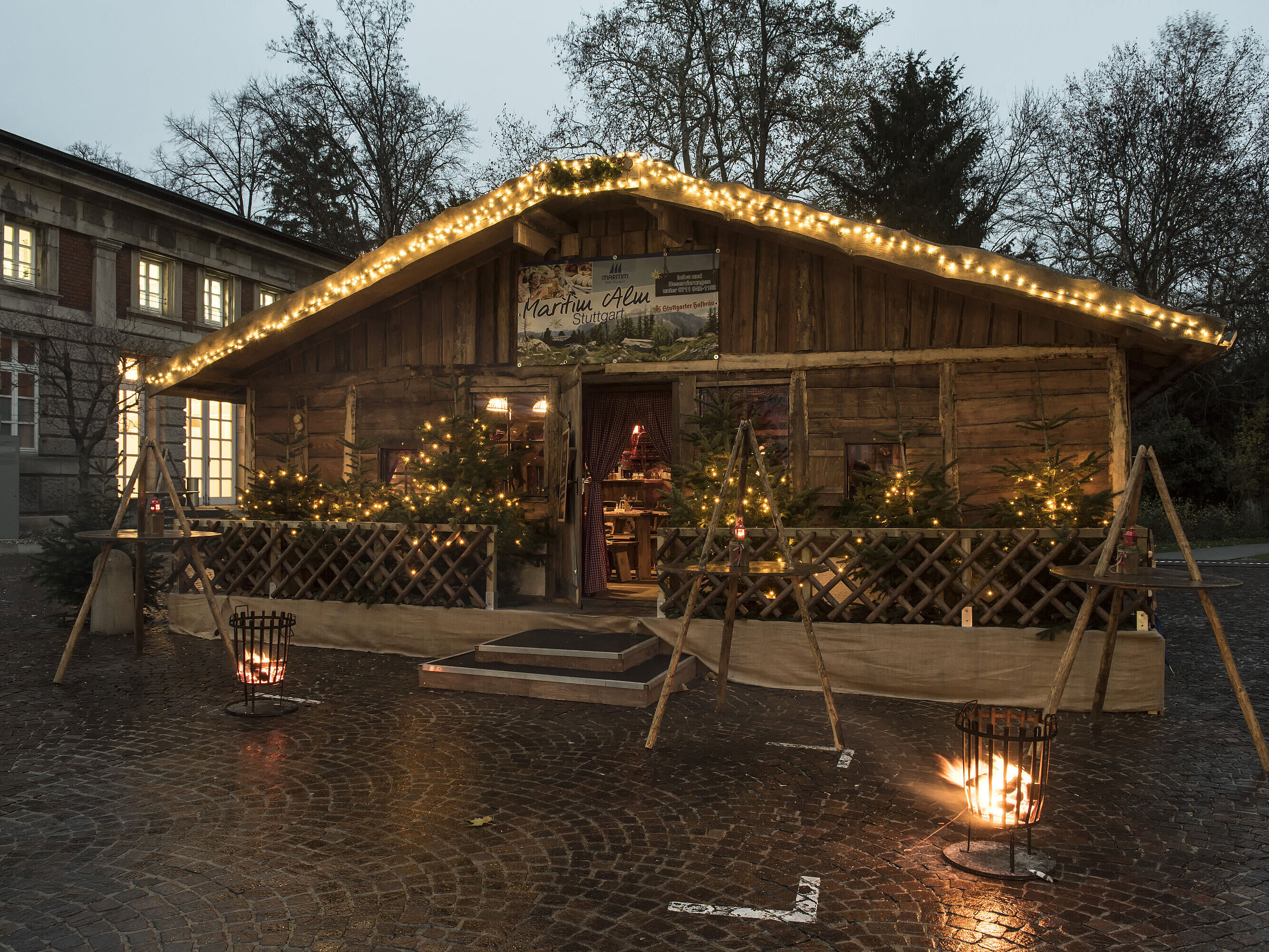 Maritim Alm Stuttgart at dusk with Christmas lights, fir trees and fire baskets in front of Maritim Hotel