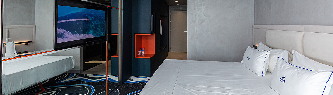 Camera spaziosa al Maritim Resort Marina Bay con grande specchio, TV e letto matrimoniale