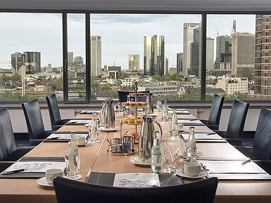 Sala de reuniones en el Maritim Hotel Frankfurt con vistas al skyline. Mesa elegante con bebidas y aperitivos para reuniones.