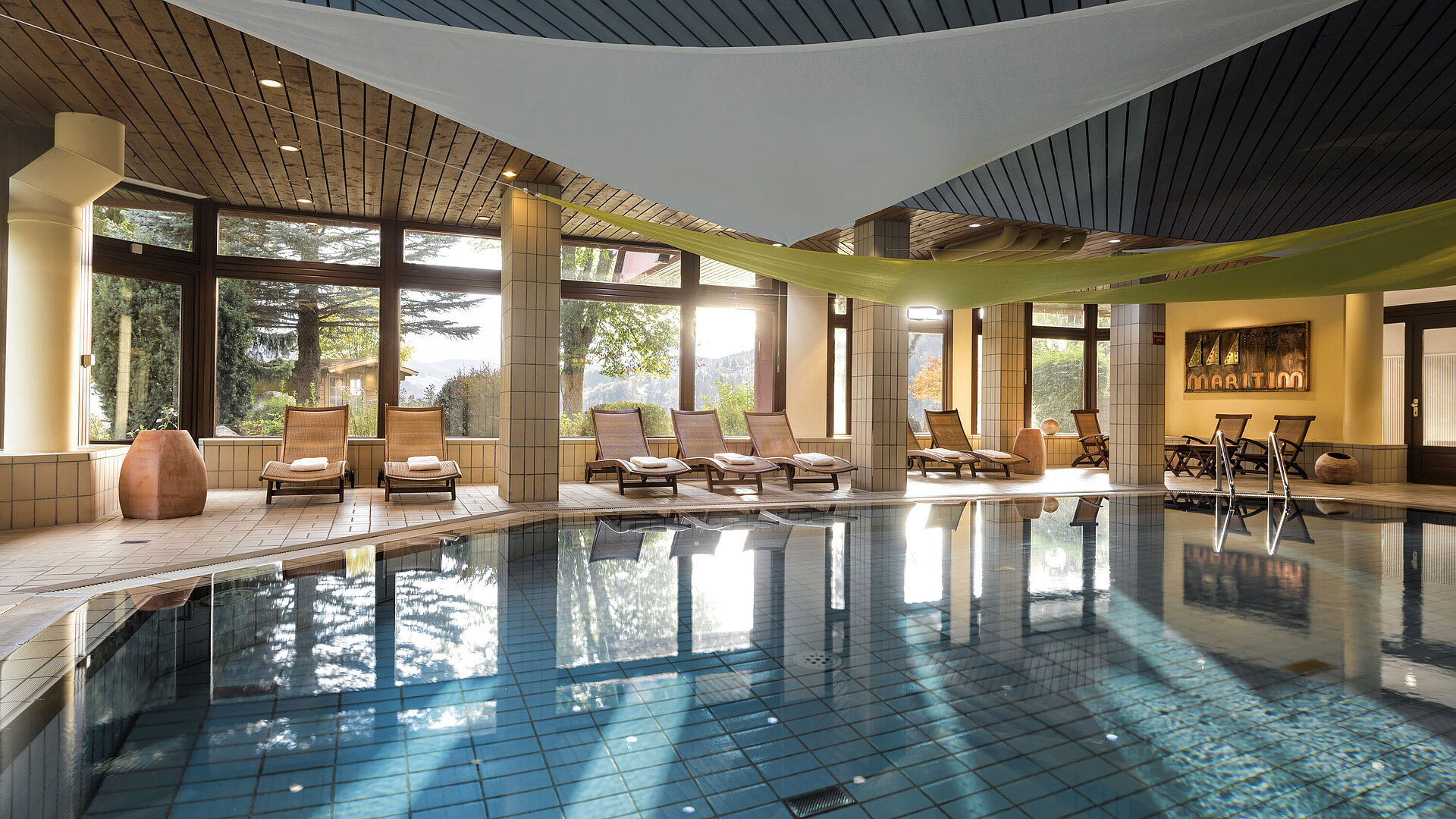 Piscina cubierta luminosa con tumbonas y vista al jardín en el Maritim Hotel Titisee