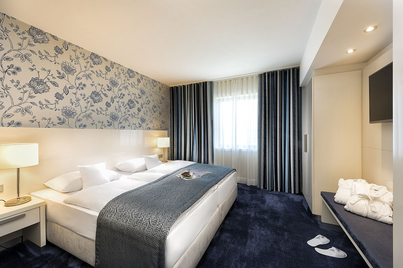 Elegante suite en el Hotel Maritim Bonn con una cama grande, colcha azul y decoración con estilo.