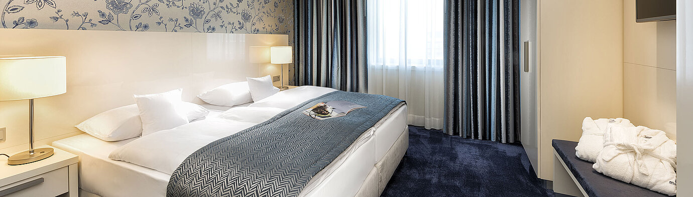 Elegante suite en el Hotel Maritim Bonn con una cama grande, colcha azul y decoración con estilo.