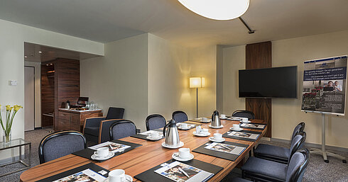 Sala con mesa de madera, sillas y equipo de presentación en el Maritim Hotel Múnich