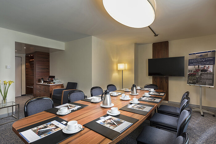 Sala con mesa de madera, sillas y equipo de presentación en el Maritim Hotel Múnich