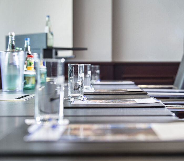 Primer plano de una mesa de conferencia elegante con vasos y blocs de notas.