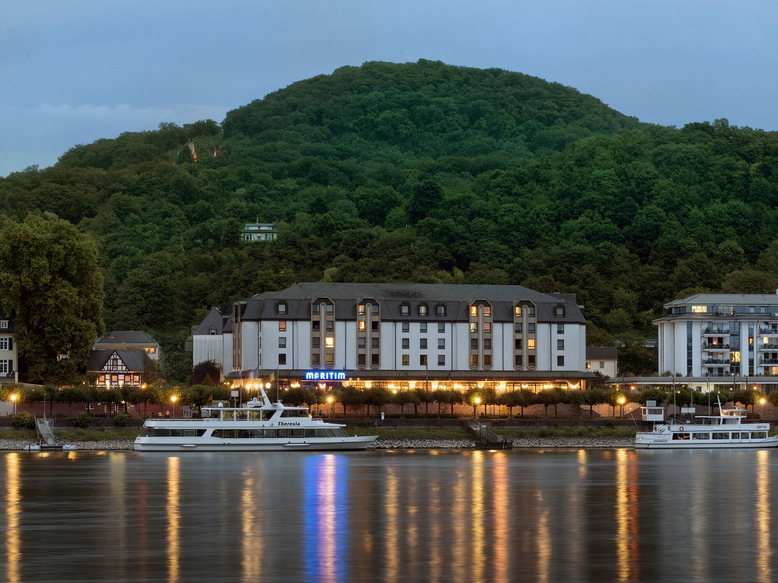 Maritim Hotel Königswinter de noche con iluminación acogedora y vistas al Rin.