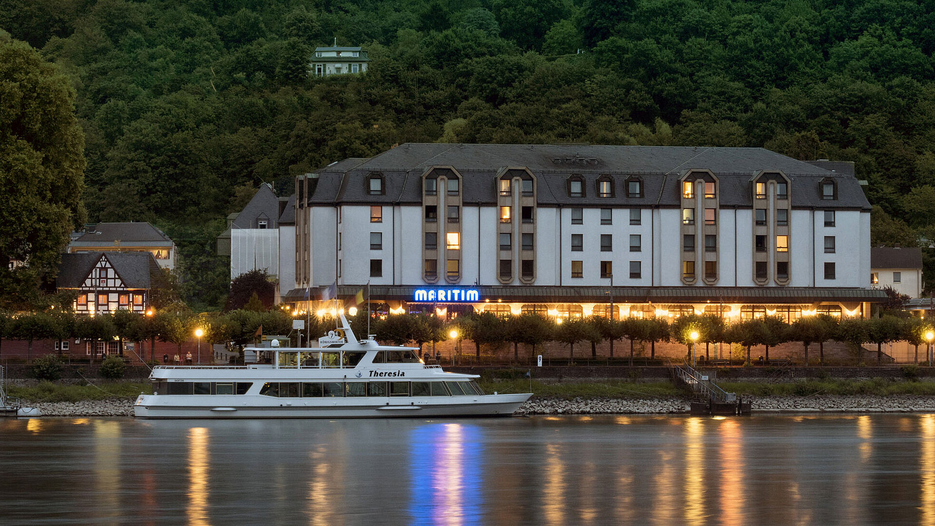 Maritim Hotel Königswinter de noche con iluminación acogedora y vistas al Rin.
