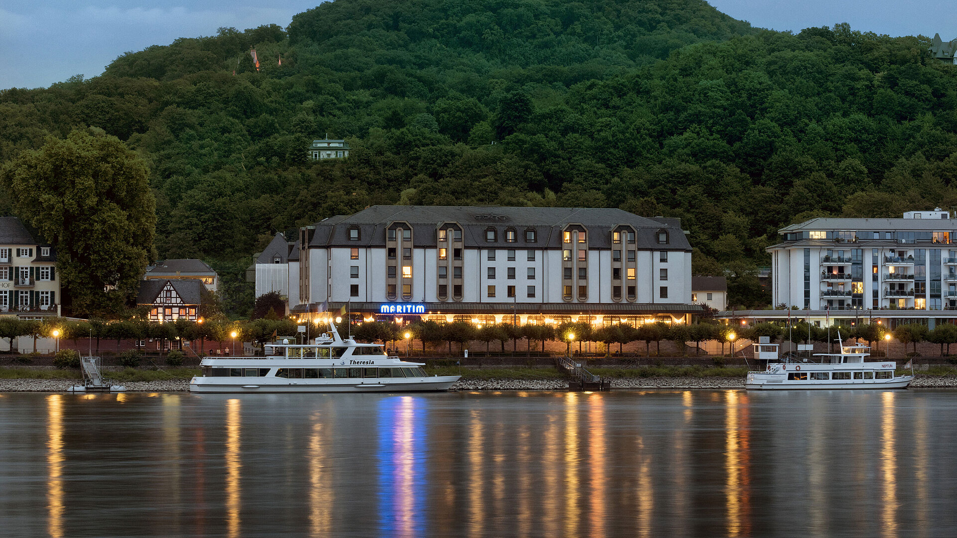 Maritim Hotel Königswinter di notte con illuminazione suggestiva e vista sul Reno.