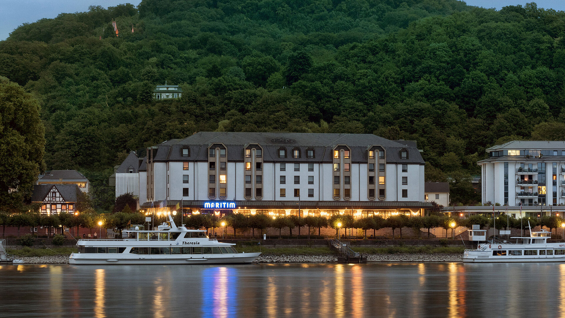 Maritim Hotel Königswinter di notte con illuminazione suggestiva e vista sul Reno.