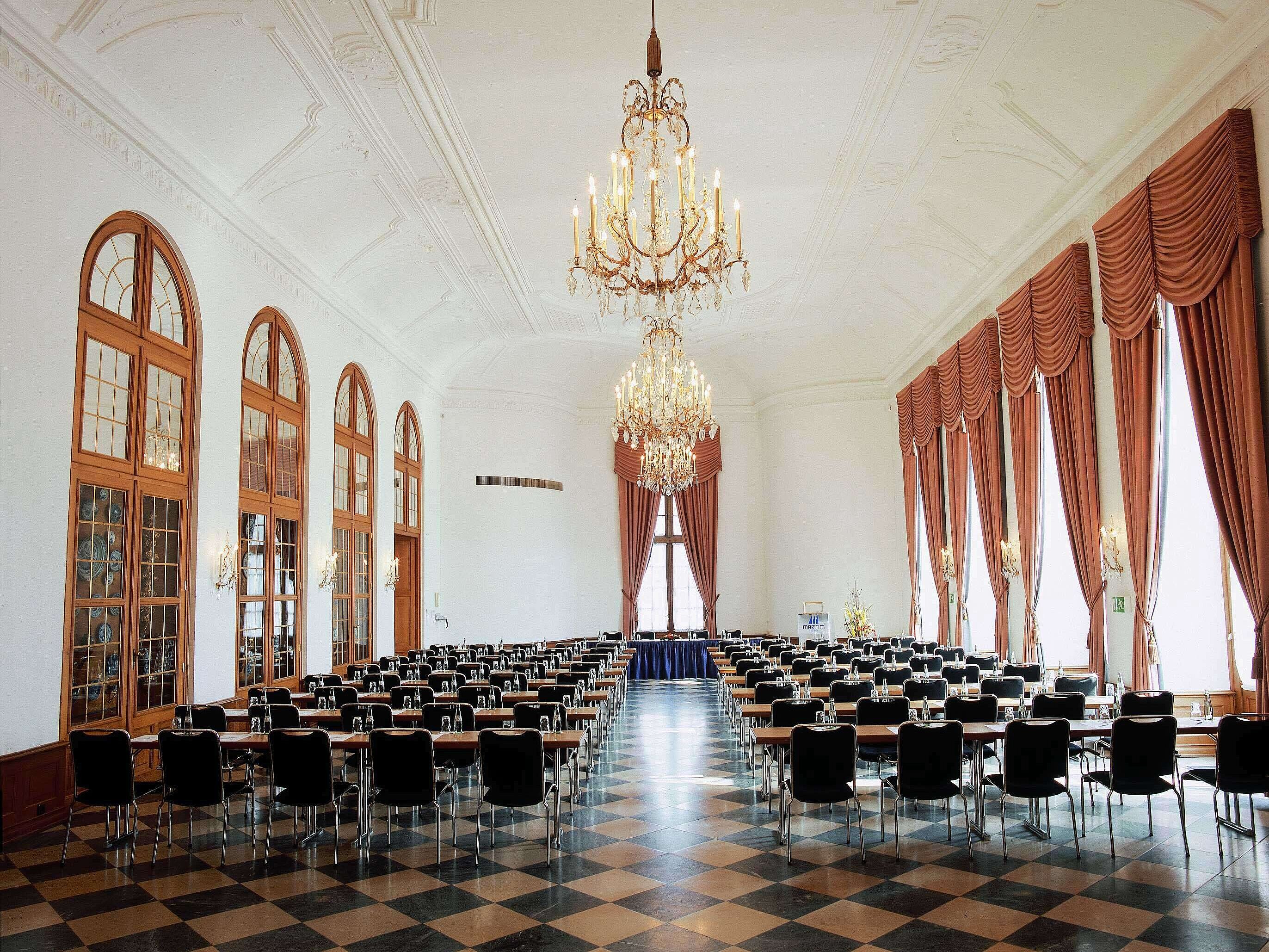 Sala eventi elegante al Maritim Hotel Fulda con lampadari, finestre alte e posti a sedere raffinati per eventi.
