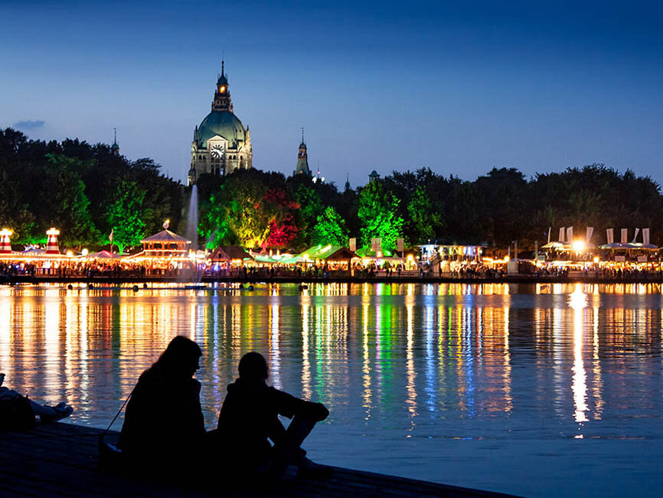 © Sebastian Grote - AdobeStock.com Festa del Maschsee ad Hannover di notte con lungolago illuminato e riflessi sull’acqua