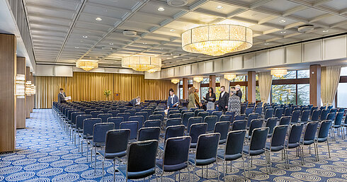 Saal Maritim en el Maritim Hotel Kiel, gran sala de conferencias con asientos en fila, lámparas de araña y escenario, el personal prepara la sala.