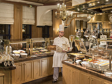 Buffet de desayuno en el restaurante "Rôtisserie" del Maritim Hotel Bonn con una variedad de platos y un chef amable.