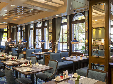 Elegant restaurant at the Maritim Hotel Darmstadt with set tables, large windows, and staff members in conversation.