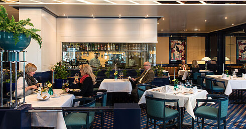 Due ospiti che gustano il pranzo nel ristorante dell'Hotel Maritim Magdeburgo, con vista sul bar e la cucina sullo sfondo.