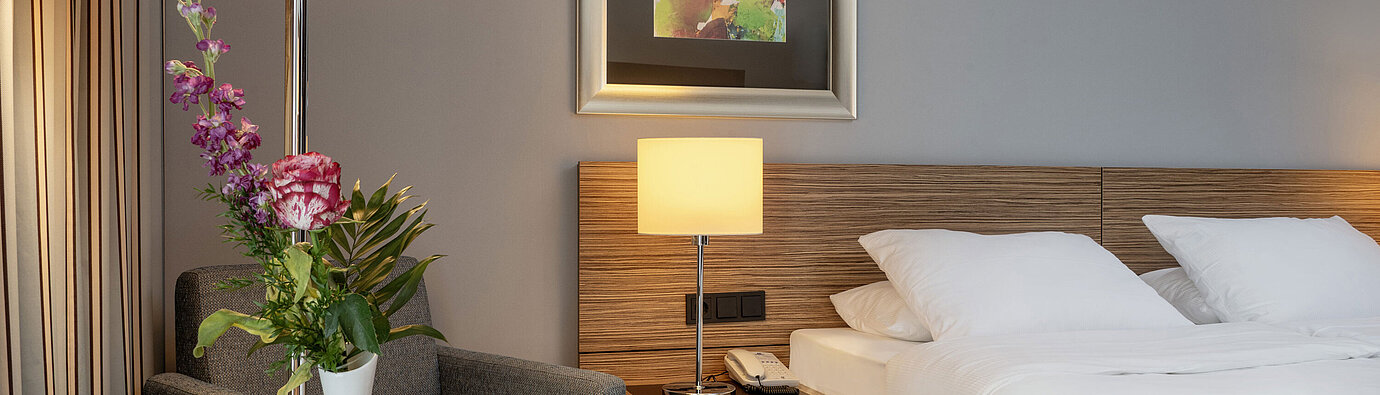 Accogliente angolo salotto con vaso di fiori accanto al comodo letto nella camera Superior del Maritim Hotel Darmstadt