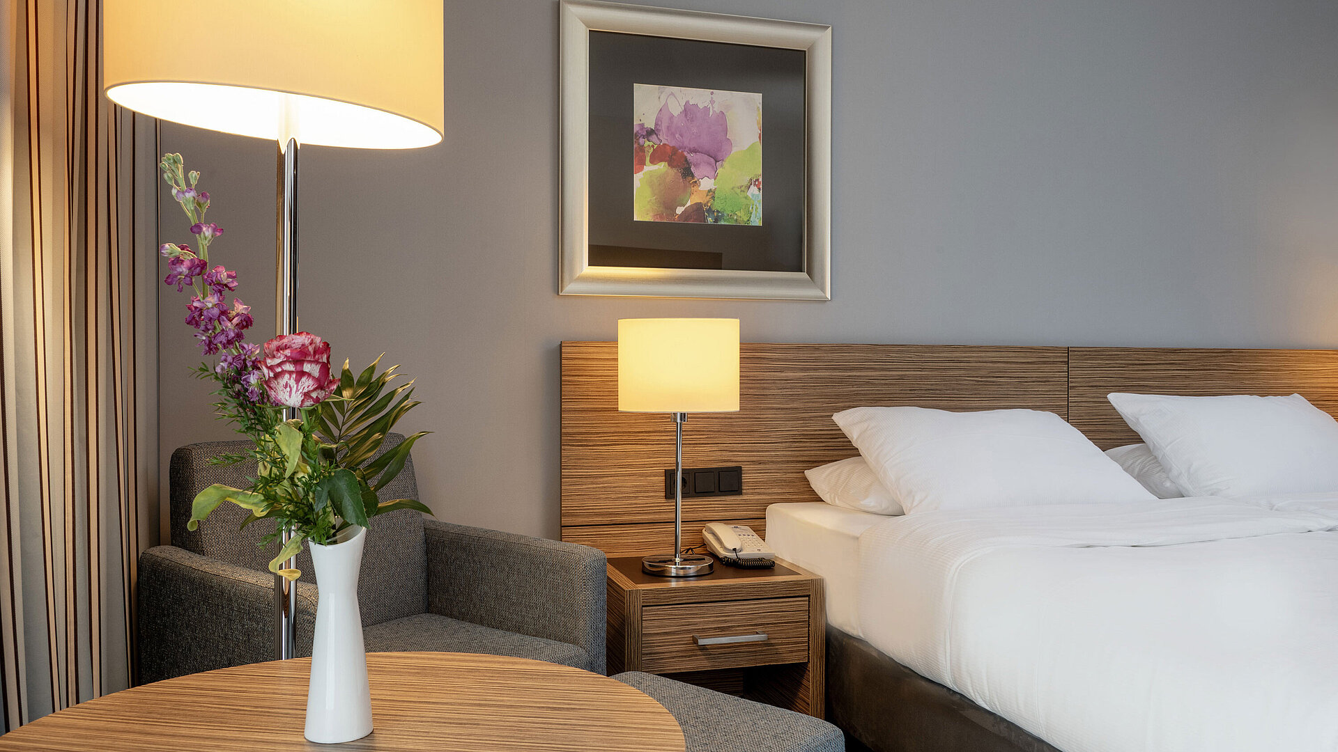 Acogedora zona de estar con un jarrón de flores junto a la cómoda cama en la habitación Superior del Maritim Hotel Darmstadt