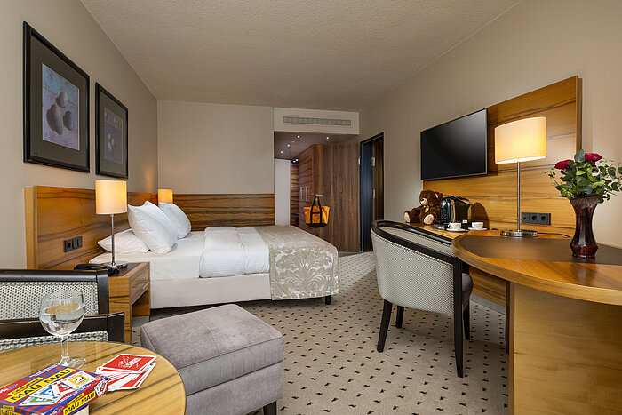 Habitación confort en el Maritim Hotel Bad Homburg con cama doble, cartas, oso de peluche y decoración de madera.
