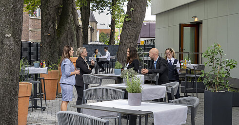 Terraza moderna del hotel Maritim Darmstadt con invitados relajándose, árboles al fondo y elegantes muebles grises.