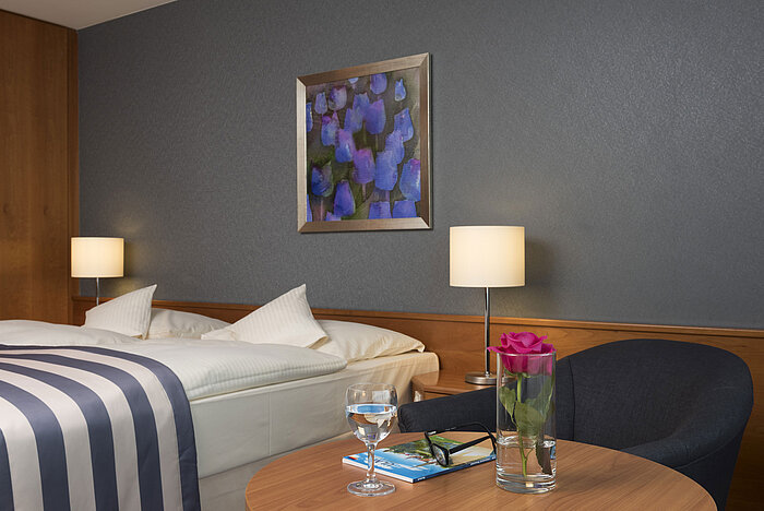 Détail au Maritim Hotel Ulm : rose, eau, lunettes et brochure de voyage près du lit